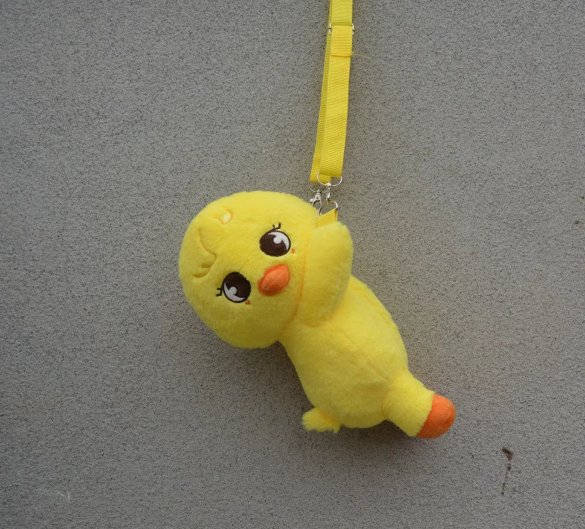 A yellow, soft stuffed toy resembling a cartoon animal character is hanging by a yellow strap against a gray background.