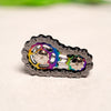 A close-up of a rainbow iridescent sprocket fidget spinner made of zinc alloy resting on a light surface.