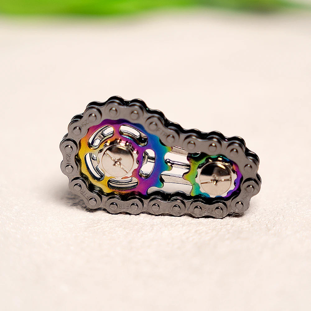 A close-up of a rainbow iridescent sprocket fidget spinner made of zinc alloy resting on a light surface.
