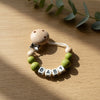 A wooden baby pacifier clip featuring custom name beads and a clip for a baby.