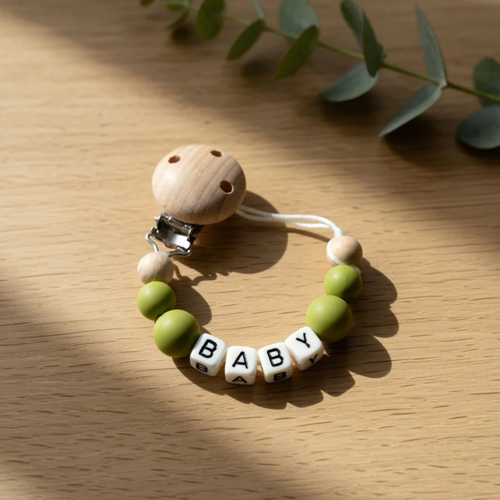 A wooden baby pacifier clip featuring custom name beads and a clip for a baby.