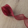 A roll of sheer, reddish-pink organza ribbon lying on a wooden surface.