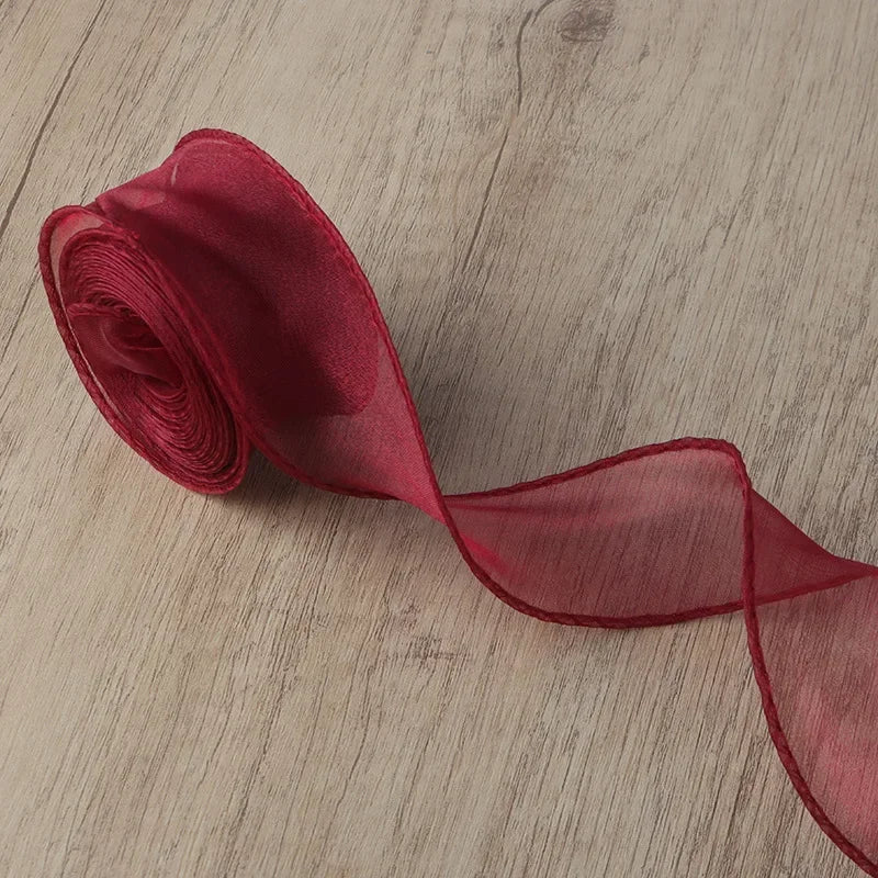 A roll of sheer, reddish-pink organza ribbon lying on a wooden surface.