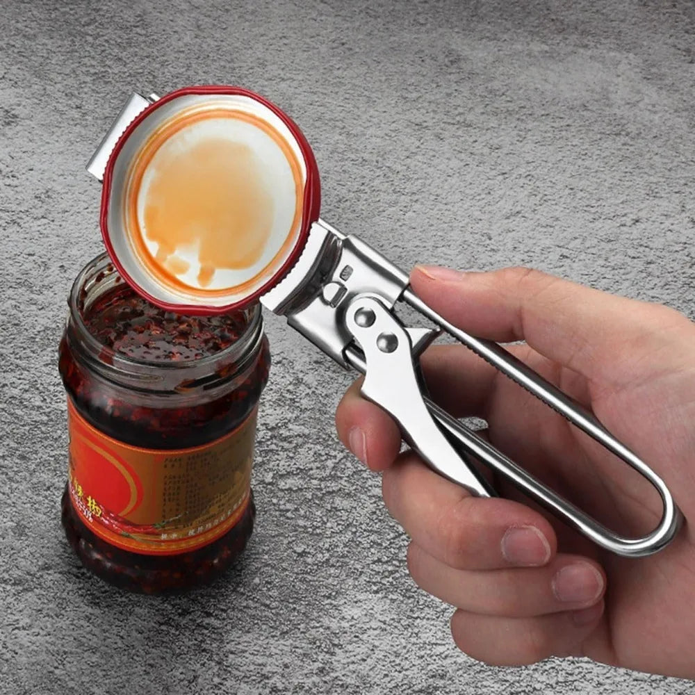 A hand holds an adjustable stainless steel can opener, positioned next to a glass jar of preserved food with its lid open.