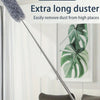 A long, retractable duster with a fuzzy head is shown next to a potted plant in a bright room.