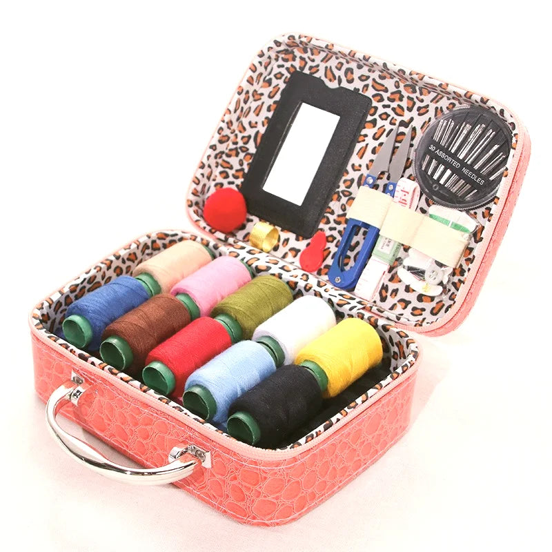 A portable faux leather sewing kit in a pink box containing various needles, thread, and tools.