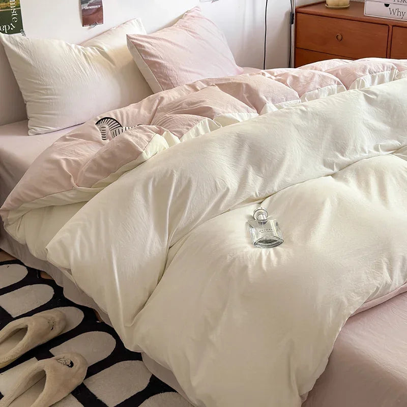 A close-up of a white and pink duvet cover set on a bed with folded bedding and light wood furniture.