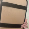 A beige plush car armrest cushion with black straps is being held by a hand.