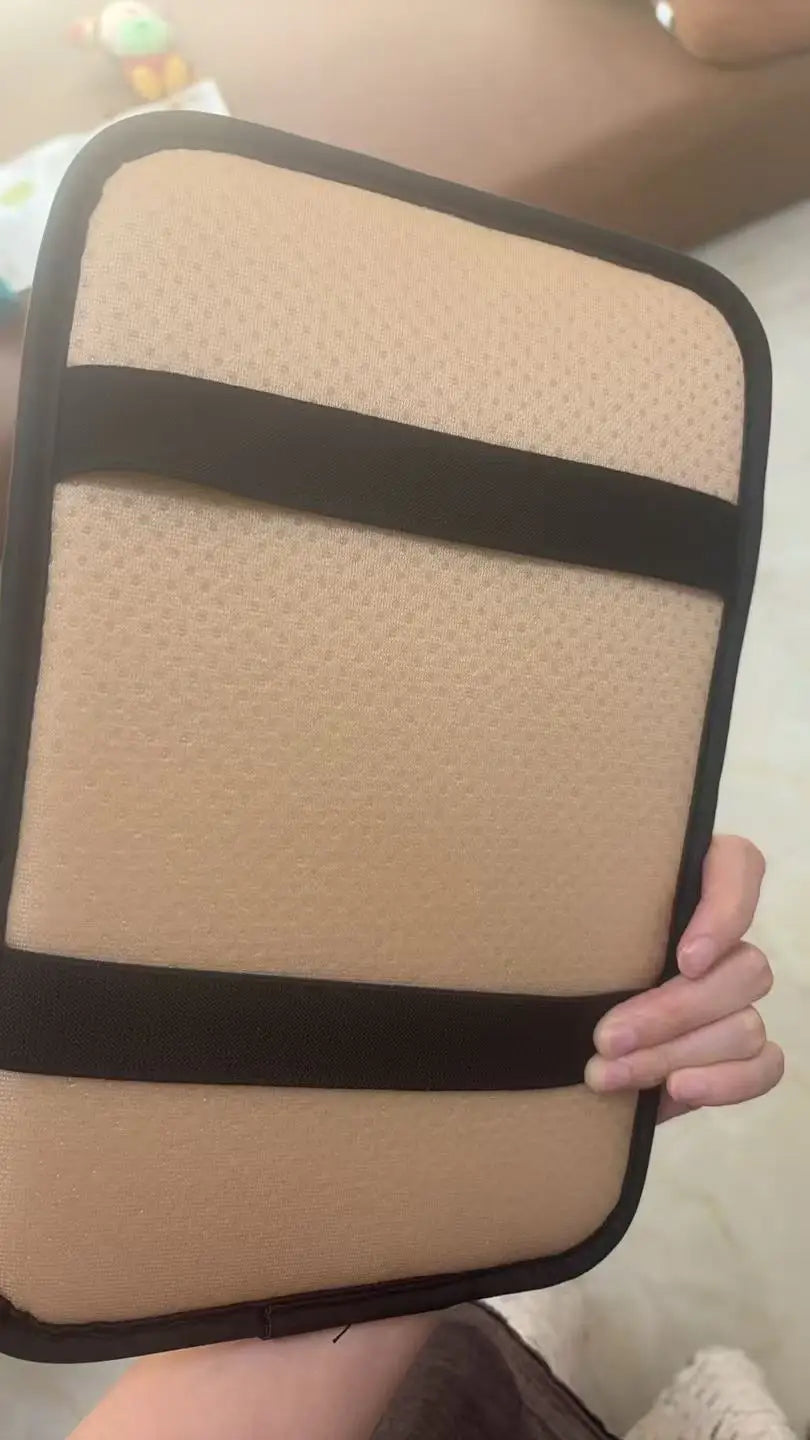 A beige plush car armrest cushion with black straps is being held by a hand.