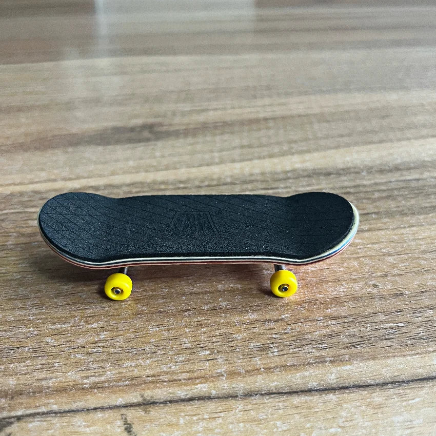 A black wooden fingerboard skateboard with yellow trucks resting on a light wooden surface.