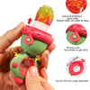 A hand is holding a pink and green rotating silicone fruit feeder with a dinosaur design, demonstrating its plug-in feature.