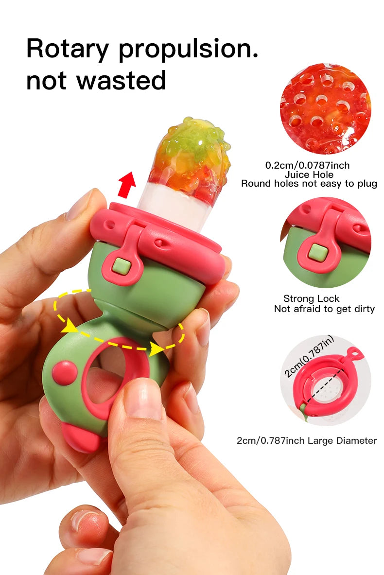 A hand is holding a pink and green rotating silicone fruit feeder with a dinosaur design, demonstrating its plug-in feature.