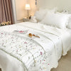 White quilted bedspread set with embroidered floral patterns on a bed in a bright bedroom.