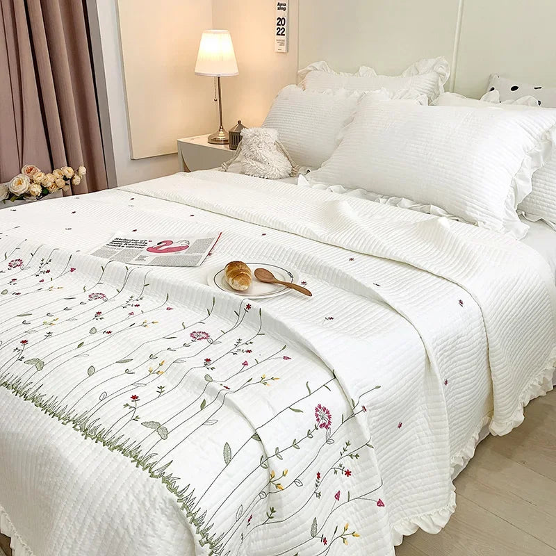 White quilted bedspread set with embroidered floral patterns on a bed in a bright bedroom.