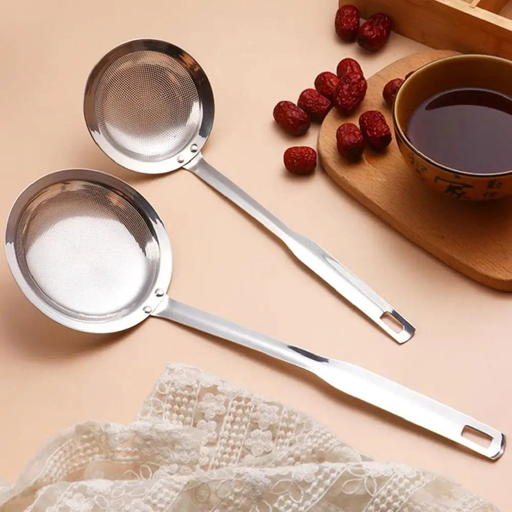 Stainless steel fine mesh skimmer spoon resting on a wooden board with red berries and a cup.