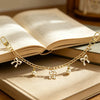Gold alloy chain necklace with pearl and bow decorations resting on an open book.