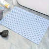 A white anti-slip shower mat with numerous massage points and drainage holes placed on a gray surface.