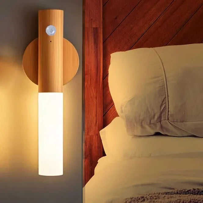 A modern magnetic LED wall light with a wooden fixture and motion sensor illuminating a bedroom setting.