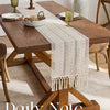 Beige boho table runner with tassels on a wooden dining table.