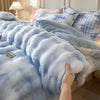A close-up view of a light blue faux fur comforter draped over a bed, with patterned pillows visible in the background.