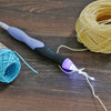A purple and black rechargeable LED crochet hook set with interchangeable heads and yarn visible on a wooden surface.