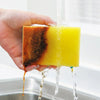 A hand holds a yellow cleaning sponge as water flows over it.