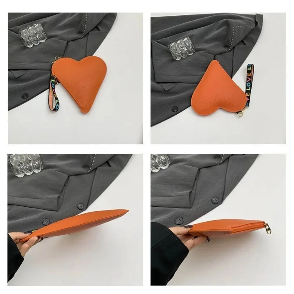 An orange heart-shaped PU coin purse with a leather wrist strap is shown against a gray jacket.