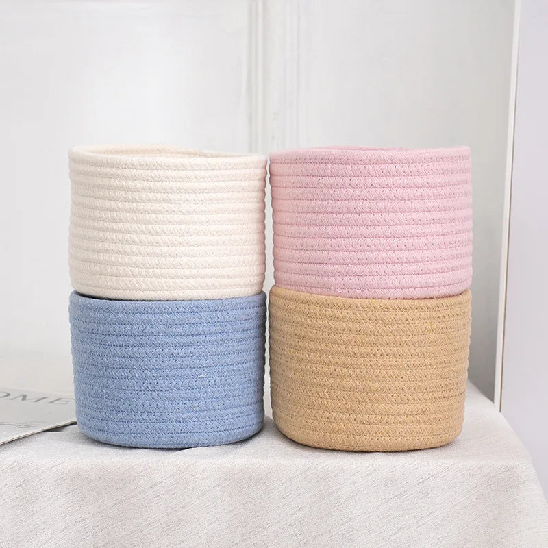 Three handwoven cotton rope storage baskets in white, pink, and beige stacked side by side.