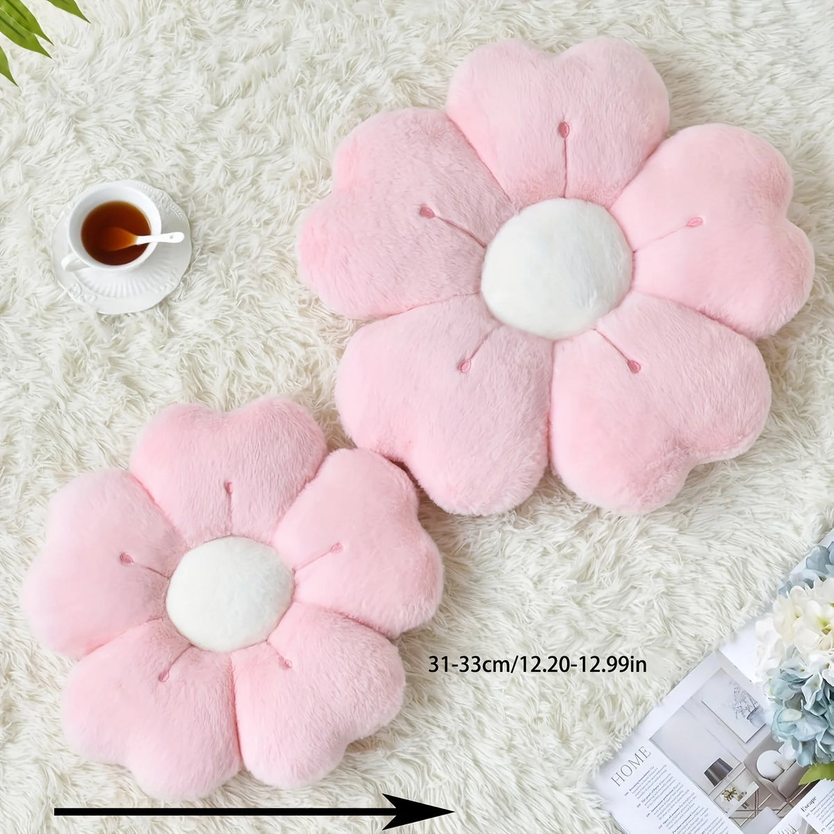 Pink plush daisy flower throw pillow with white center resting on a white fluffy surface.