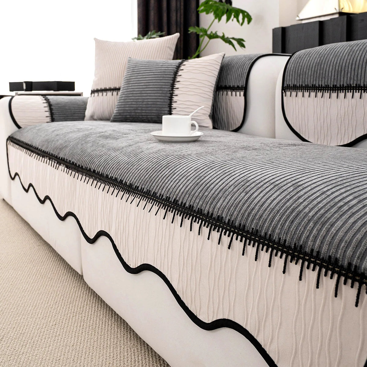 A light gray and white striped chenille sofa cover with a pleated black hem and decorative pillows.