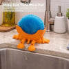 An orange 3D sponge holder with a blue sponge inside is hanging over a kitchen sink.