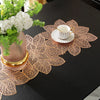 A set of ornate gold-colored PVC table runners and placemats with intricate floral designs on a black table.