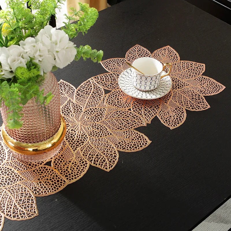 A set of ornate gold-colored PVC table runners and placemats with intricate floral designs on a black table.