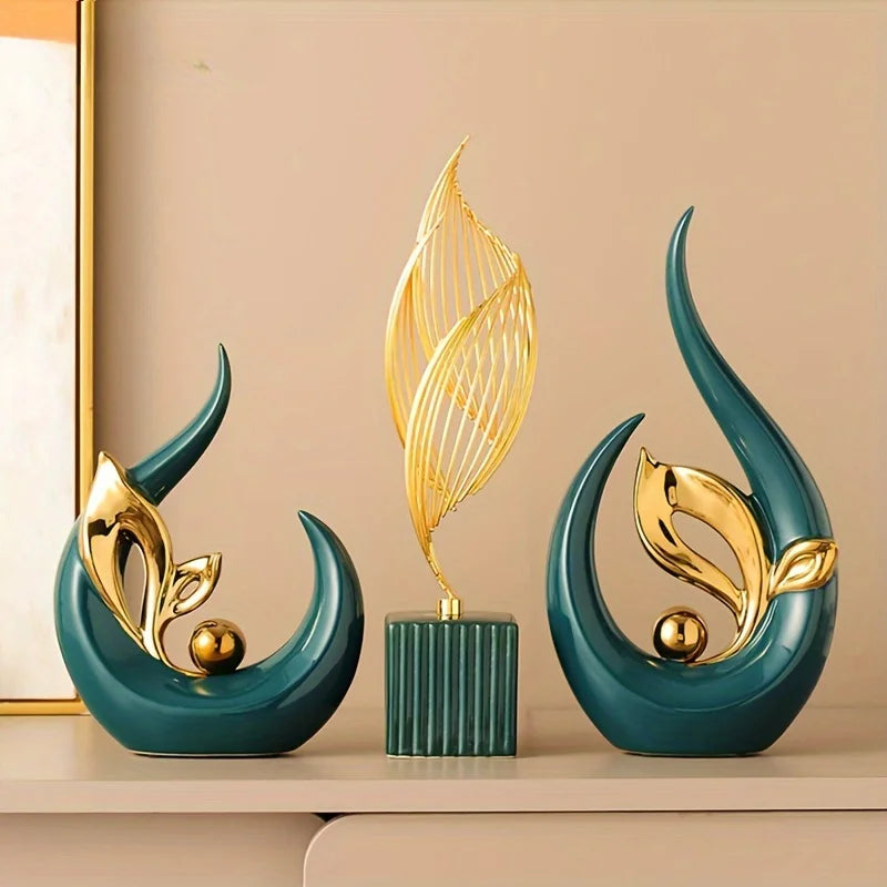 Three modern ceramic sculptures in teal and gold featuring leaf shapes displayed on a light surface.