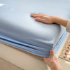 A hand is gently touching a light blue fitted sheet on a bed.