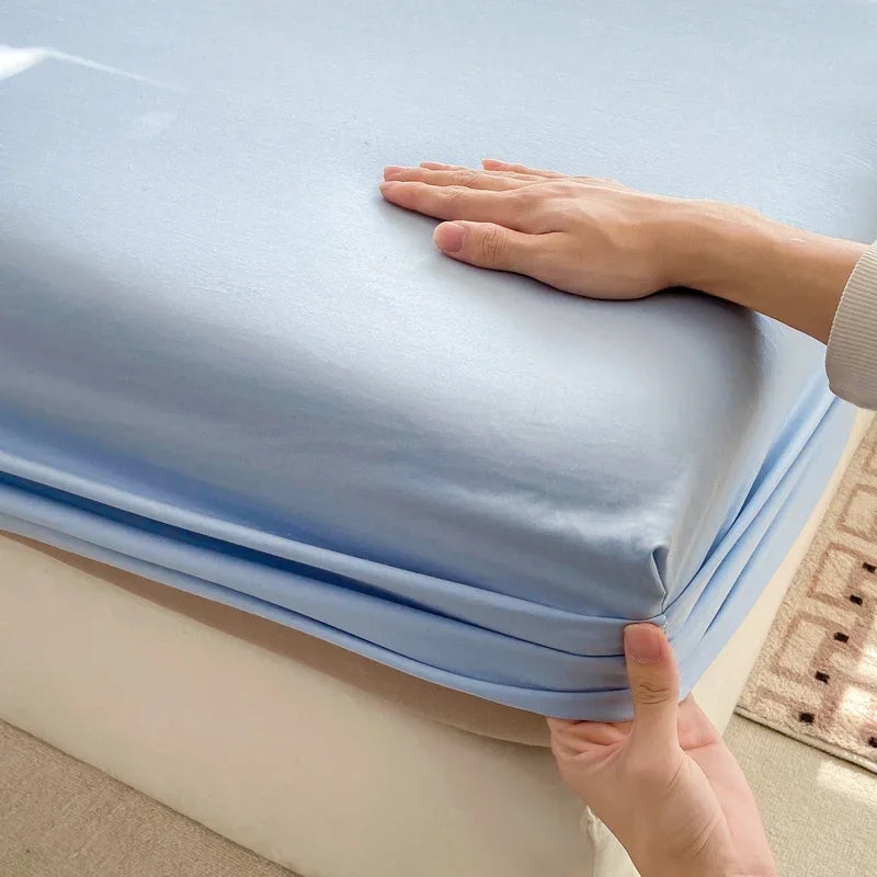 A hand is gently touching a light blue fitted sheet on a bed.
