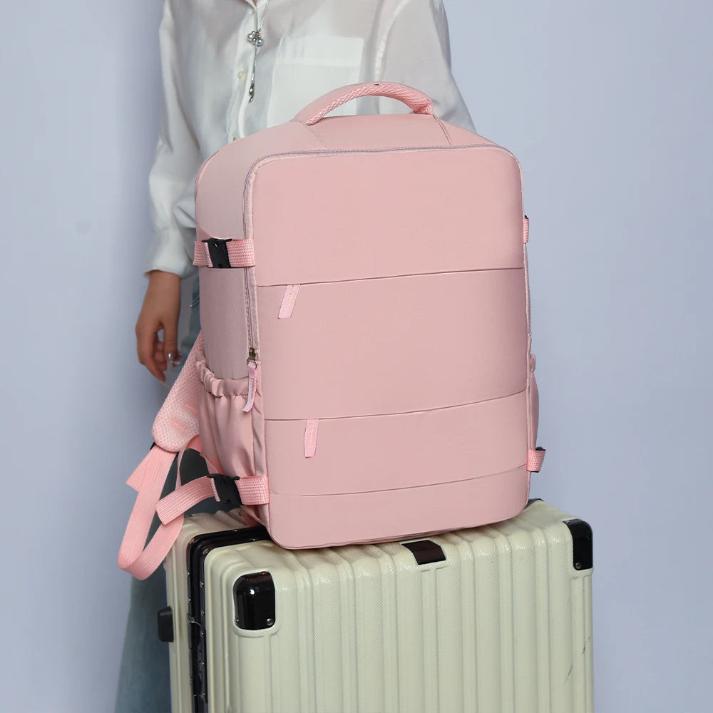 A pink compact travel backpack resting on top of a light-colored suitcase.