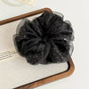 A black polka dot mesh scrunchie hair tie is displayed on a wooden tray.