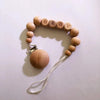 A wooden bracelet spelling out BABY with small wooden beads and a silicone pacifier clip attached.