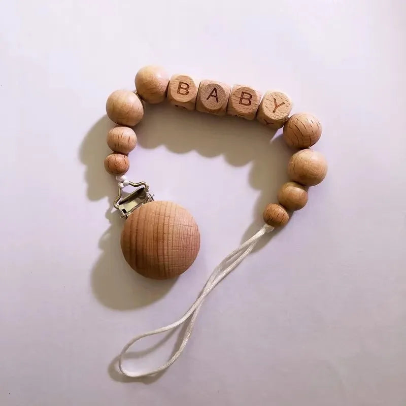 A wooden bracelet spelling out BABY with small wooden beads and a silicone pacifier clip attached.