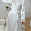 A white silk satin robe with lace trim and long sleeves is displayed indoors.