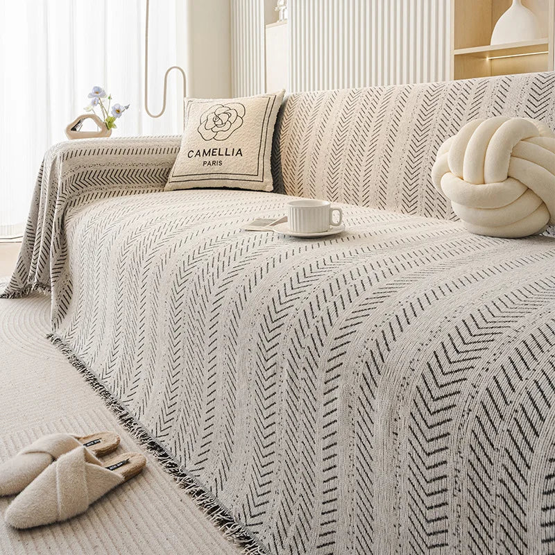 Beige und schwarz gemusterter Sofabezug mit cremefarbigem Kissen und weißer Tasse auf einem hellen Bett.