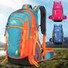 A bright orange and blue hiking backpack is shown outdoors on a grassy field.