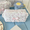 A white cosmetic pouch with a vintage rose print and pink lace trim rests on a blue wooden surface.