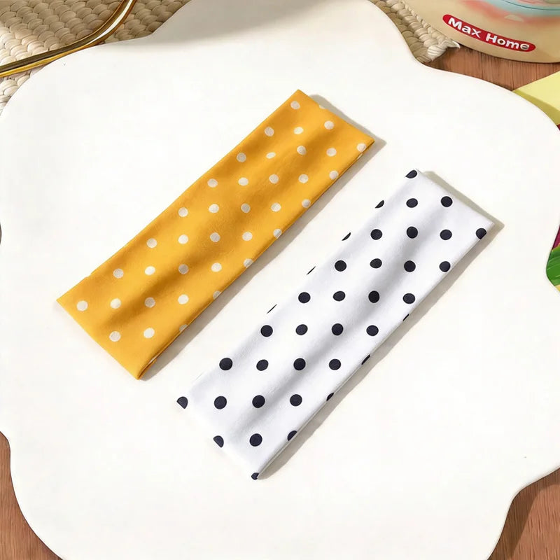Deux bandeaux de tissu sont exposés sur une surface blanche : un jaune à pois blancs et un blanc à pois noirs.