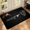 A black anti-slip doormat featuring a silver stylized logo on a light wooden floor.