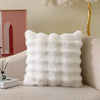 A fluffy white decorative pillow cover with vertical pleats resting on a light-colored sofa.