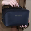 A black leather travel makeup organizer bag being held by a hand against a beige jacket.