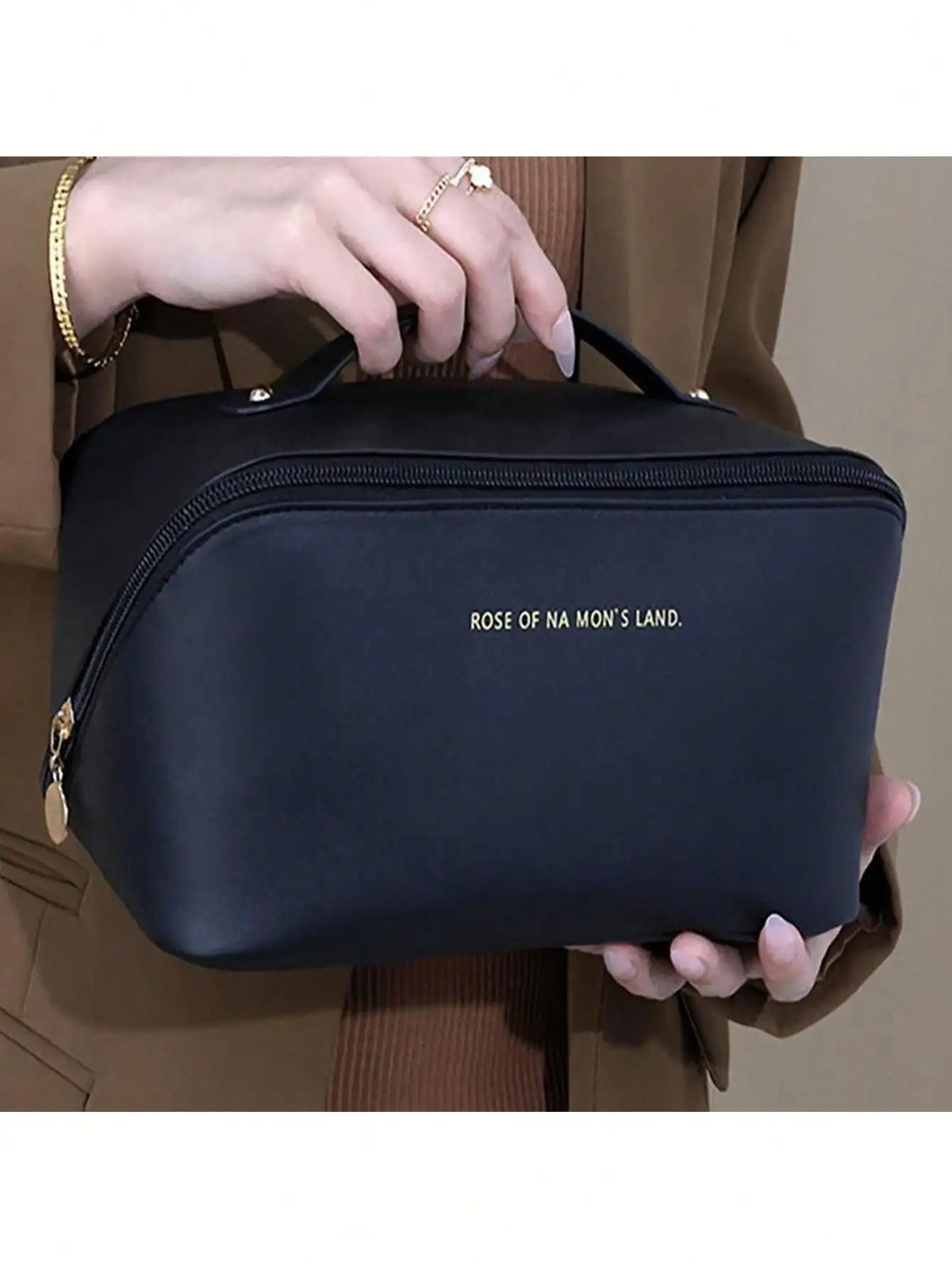 A black leather travel makeup organizer bag being held by a hand against a beige jacket.