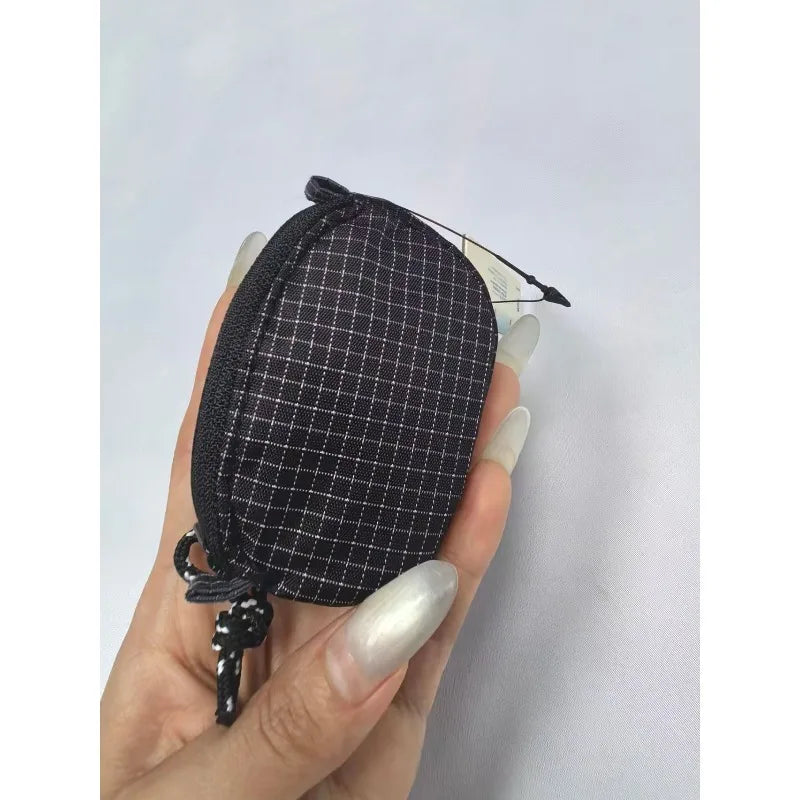 Une main tient un étui et une pochette de clés pour écouteurs en nylon à carreaux noirs.
